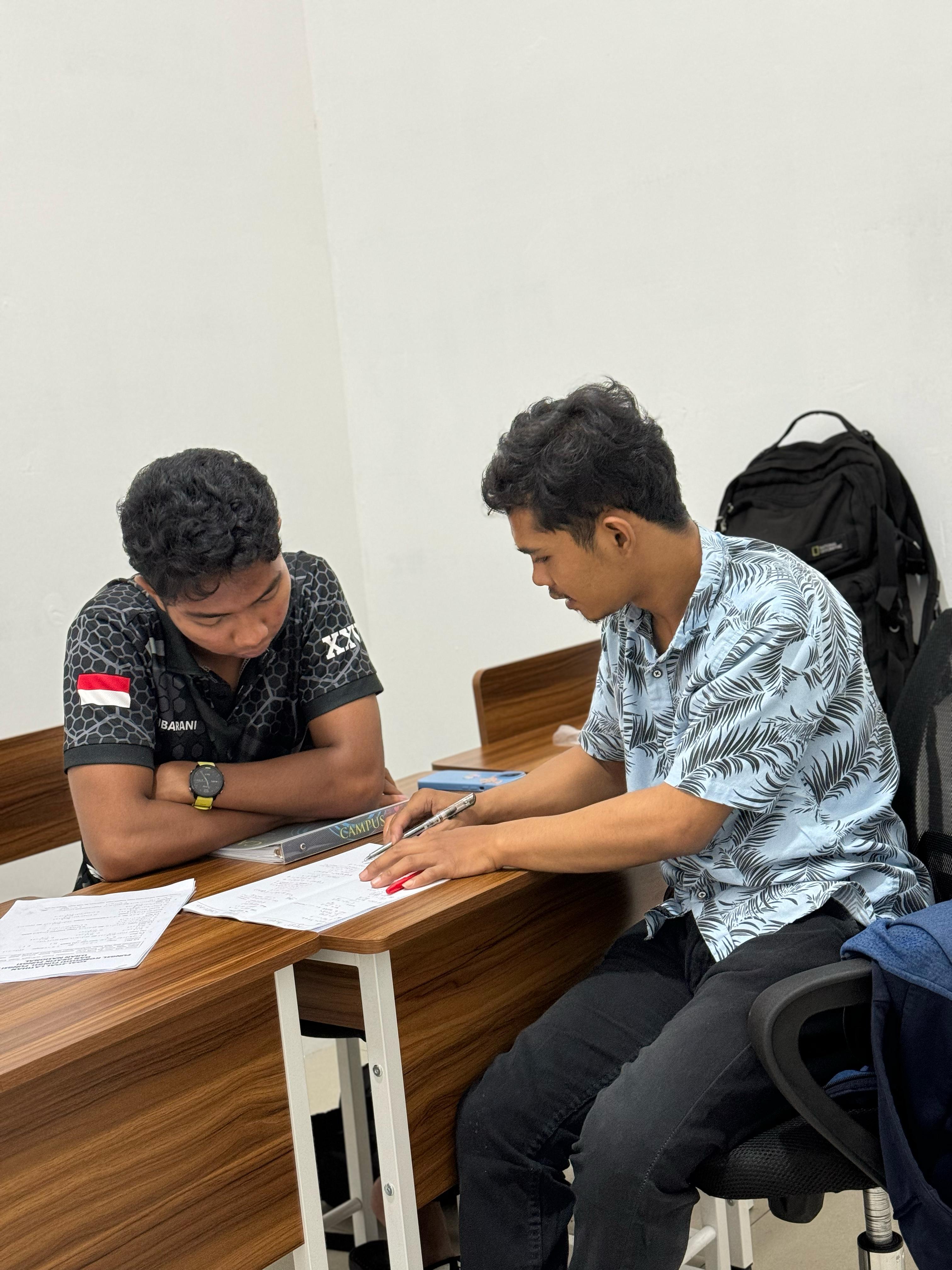 Dua siswa saling membahas jawaban latihan soal di ruang kelas
